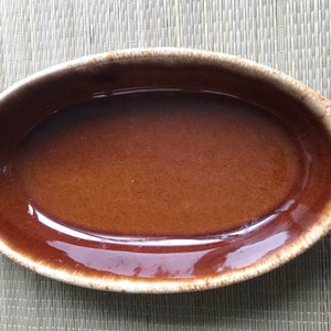 May include: A brown oval ceramic baking dish with a glazed interior and a speckled exterior. The dish has two handles on the sides.