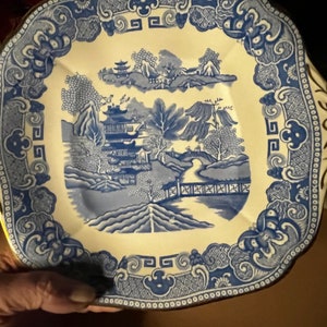 May include: A blue and white porcelain plate with a decorative design of a Chinese garden scene. The plate has a scalloped edge and a gold trim.