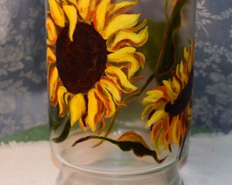 Könnte beinhalten: Eine klare Glasvase mit einem gemalten Design aus zwei Sonnenblumen. Die Sonnenblumen sind gelb mit braunen Zentren und grünen Blättern.
