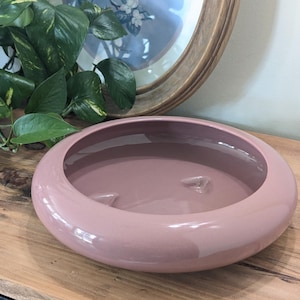 May include: A large, round, mauve-colored ceramic planter with a smooth, glossy finish. The planter has a wide, shallow bowl shape with a slightly raised rim.