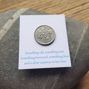 Puede incluir: Una moneda de seis peniques de plata de 1966 con el texto "FID DEF SIX PENCE" y "1966" en ella. La moneda está sobre una tarjeta blanca con el texto "Something old, something new Something borrowed, something blue and a silver sixpence in her shoe".