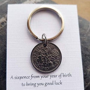 May include: A silver keychain with a sixpence coin from 1963 attached. The coin has a floral design and the text "SIX PENCE 1963" is visible. The card reads "A sixpence from your year of birth to bring you good luck."