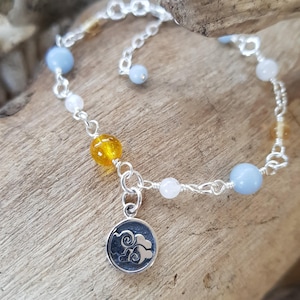 Peut inclure: Un bracelet en argent avec une chaîne, des perles bleues, blanches et jaunes et un pendentif en argent en forme de nuage.