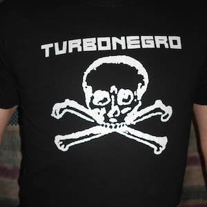 May include: Black t-shirt with a white skull and crossbones graphic and the text "TURBONEGRO" printed on the front.