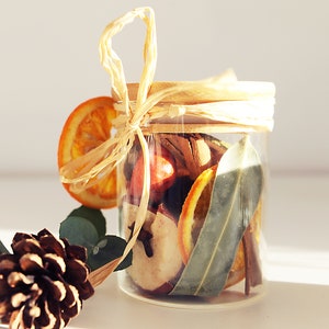 May include: A glass jar filled with dried orange slices, cinnamon sticks, bay leaves, and other spices. The jar is tied with a natural twine bow and has a wooden lid.