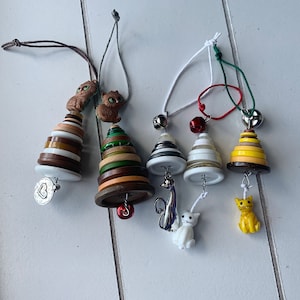May include: Five handmade Christmas decorations featuring a variety of button designs, including a cat, a tree, and a heart. The decorations are strung on white and red ribbon.