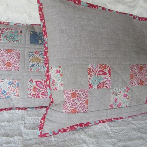 May include: Two decorative pillows with a gray linen fabric and a pink floral pattern. The pillows have a pink trim.