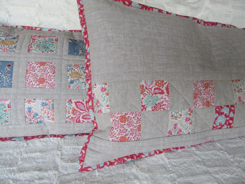 May include: Two decorative pillows with a gray linen fabric and a pink floral pattern. The pillows have a pink trim.