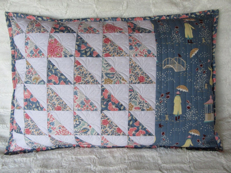 May include: A blue and white quilted pillow with a floral pattern on one side and a blue and white pattern with a bridge and people on the other side.