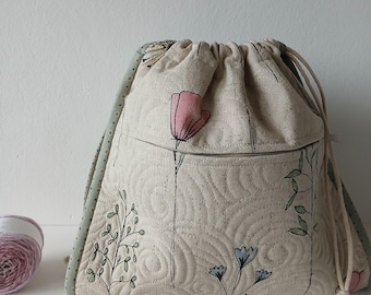 May include: A beige drawstring bag with a floral print. The bag has a green and white polka dot trim and a zippered pocket on the front. The bag is made of a soft, quilted fabric.