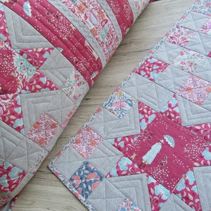 May include: Two quilted pillow covers with a star pattern in shades of pink, blue, and gray. The fabric features a floral print and a repeating image of a woman with an umbrella.