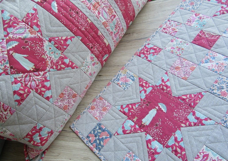 May include: Two quilted pillow covers with a star pattern in shades of pink, blue, and gray. The fabric features a floral print and a repeating image of a woman with an umbrella.