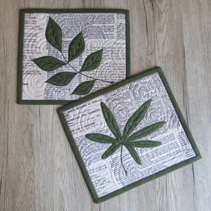 Peut inclure: Deux dessous-de-verre en tissu vert et blanc avec un motif de feuille verte. Les dessous-de-verre sont en tissu avec un motif imprimé de vieux textes. Les dessous-de-verre sont sur une surface en bois.