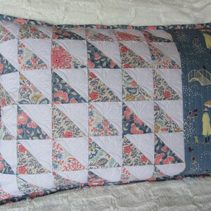 May include: A decorative pillow with a patchwork design featuring a variety of floral patterns in shades of pink, blue, and white. The pillow is quilted with a white fabric and has a blue fabric border. The back of the pillow features a blue fabric with a repeating pattern of people walking in the rain.