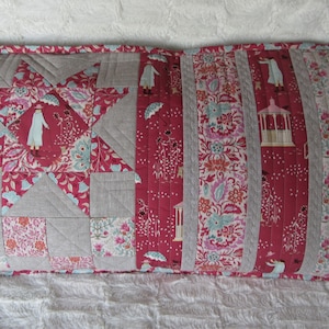 Könnte beinhalten: Ein langes rechteckiges Kissen mit Patchwork-Muster. Das Kissen besteht aus verschiedenen Stoffen in Rot-, Grau- und Weißtönen. Die Vorderseite des Kissens zeigt ein Sternmuster mit einem Blumenmuster. Die Rückseite des Kissens ist aus einfarbigem rotem Stoff.