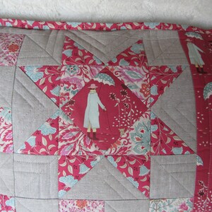 May include: A gray and pink patchwork pillow with a star design. The star is made of different fabrics with floral patterns. The pillow has a gray border and a pink trim.