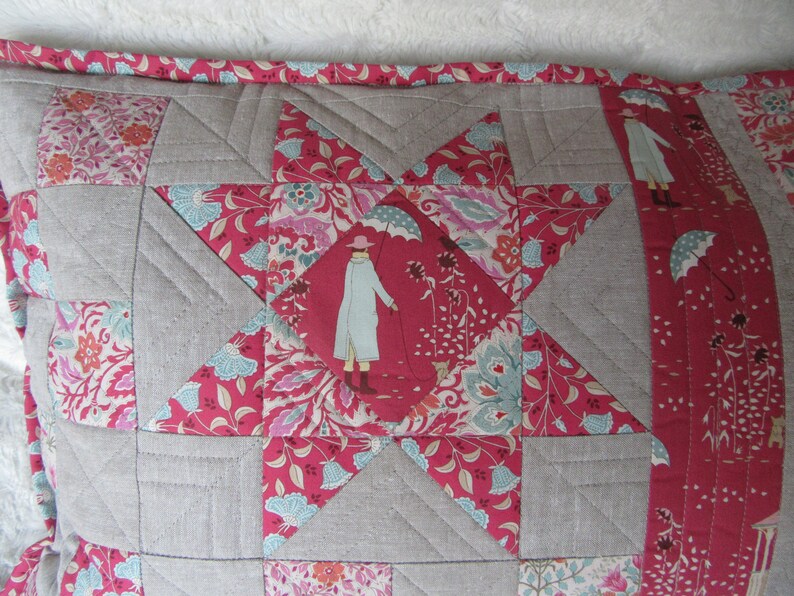 May include: A gray and pink patchwork pillow with a star design. The star is made of different fabrics with floral patterns. The pillow has a gray border and a pink trim.