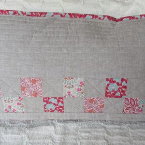 May include: A long rectangular pillow with a light gray linen fabric cover. The pillow has a pink and white floral patterned border and a bottom row of patchwork squares in pink, white, and blue floral patterns.