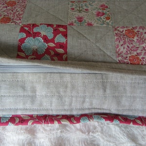 May include: A gray linen cushion with a zipper closure and a patchwork design featuring floral patterns in shades of pink, red, and blue.