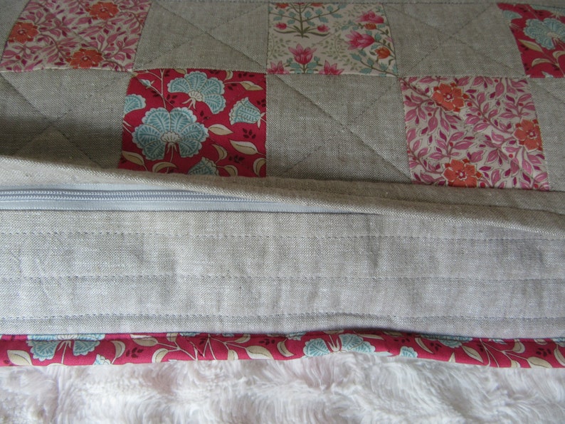 May include: A gray linen cushion with a zipper closure and a patchwork design featuring floral patterns in shades of pink, red, and blue.