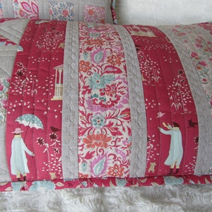 May include: A red and white patterned pillow with a gray linen border. The pillow is quilted with a floral design and features a small figure holding an umbrella.