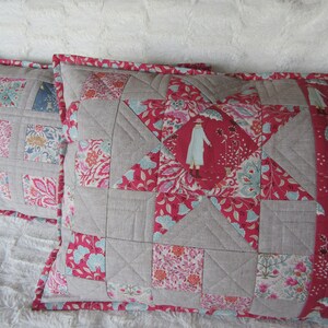 May include: Two decorative pillow covers with a patchwork design. The pillow covers are made of a variety of fabrics, including linen and cotton. The pillow covers feature a star design and a floral pattern. The pillow covers are in shades of pink, red, and gray.