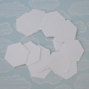 May include: A pile of white hexagon-shaped paper pieces on a light blue background with a white cloud pattern.