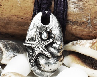 May include: Silver pendant necklace featuring a detailed sculpted seashell with a starfish on top. The pendant is hanging from a black cord and is surrounded by seashells.