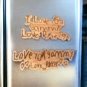May include: Two wooden signs with handwritten messages on a silver refrigerator. The top sign says "I love you gammy Love Ryleigh 2023". The bottom sign says "Love you gammy Love Parker 2023".