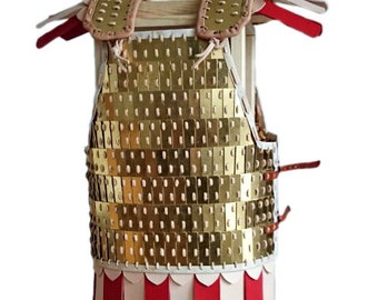 May include: A gold lamellar armor with red and white leather strips hanging from the bottom. The armor is displayed on a wooden stand.