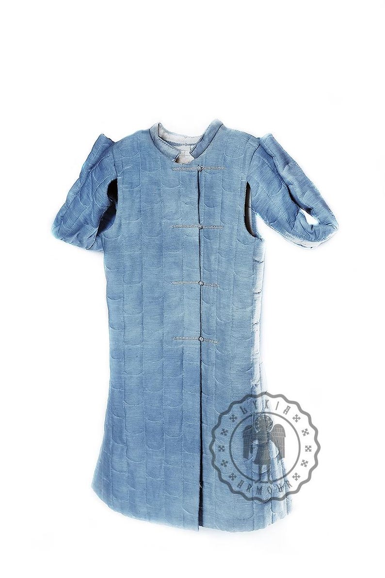 Puede incluir: Una prenda acolchada azul con mangas largas y cierre de botones. La prenda tiene un logotipo "LYKIA ARMOUR" en la parte inferior derecha.