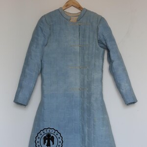 Puede incluir: Una chaqueta acolchada azul claro con cuello alto y un solo bot&oacute;n de cierre. La chaqueta tiene una silueta larga y ajustada y est&aacute; colgada de una percha de madera. La chaqueta tiene un logotipo en la parte inferior izquierda que dice "Byrkia Armour".