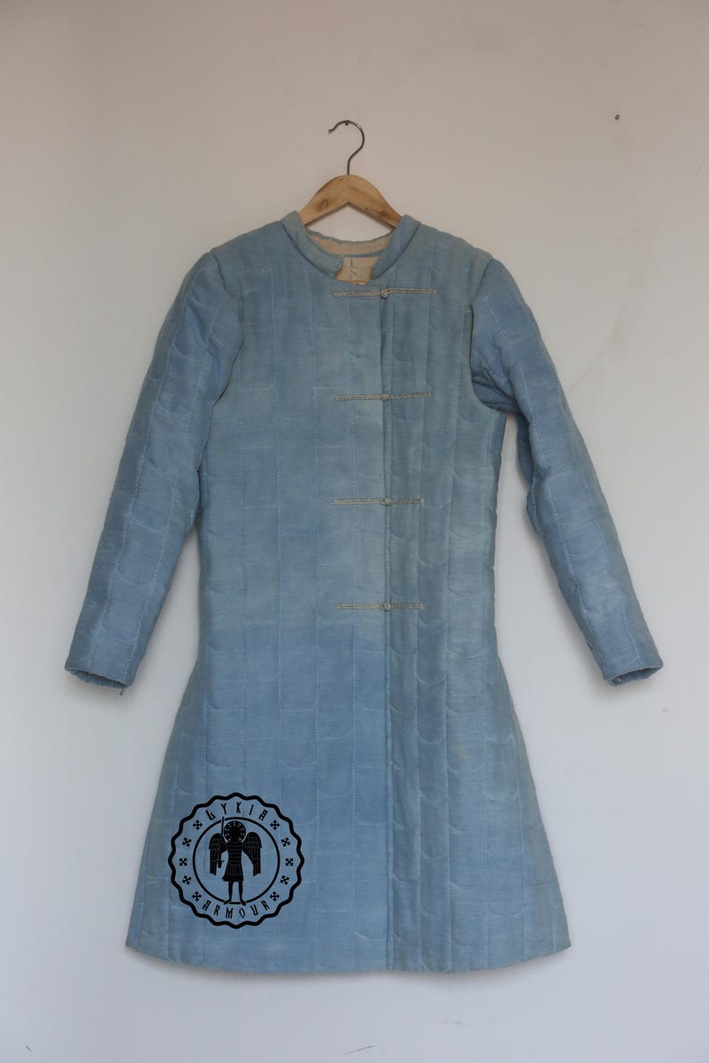 Puede incluir: Una chaqueta acolchada azul claro con cuello alto y un solo bot&oacute;n de cierre. La chaqueta tiene una silueta larga y ajustada y est&aacute; colgada de una percha de madera. La chaqueta tiene un logotipo en la parte inferior izquierda que dice "Byrkia Armour".