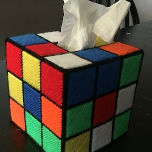 May include: A tissue box cover shaped like a Rubik's Cube with a white tissue box inside. The cube is made of colorful squares in red, blue, green, yellow, orange, and white.