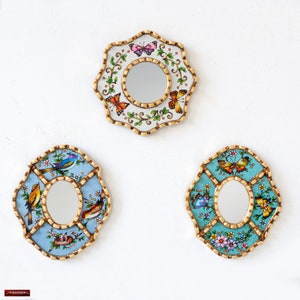May include: Three decorative mirrors with ornate gold frames and painted floral and bird designs. The mirrors are round and oval shaped and have a white, blue, and turquoise background.