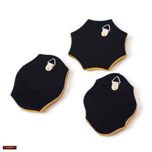 May include: Three black wall decor pieces with gold trim and a unique shape. Each piece has a metal hanger on the back for easy installation. The pieces are set against a white background.