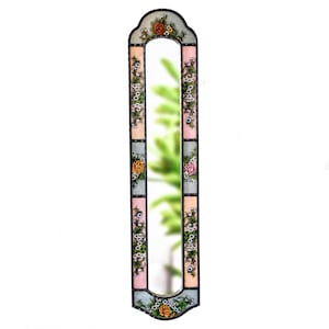 May include: A tall, rectangular mirror with a decorative frame featuring a floral design. The frame is painted in shades of pink, blue, and green, with flowers and leaves in various colors. The mirror has a slightly arched top and bottom.