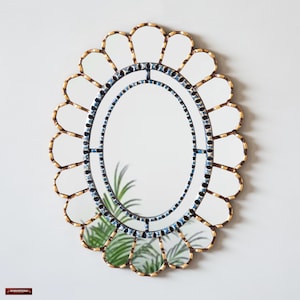 Può includere: Specchio decorativo ovale con bordo smerlato. La cornice è dorata e presenta un bordo a mosaico blu e nero. La forma dello specchio ricorda un fiore.