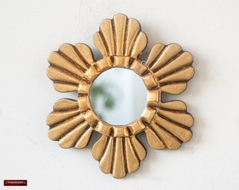 May include: A gold-toned, decorative wall mirror with a flower-shaped frame. The mirror has a round, reflective surface.