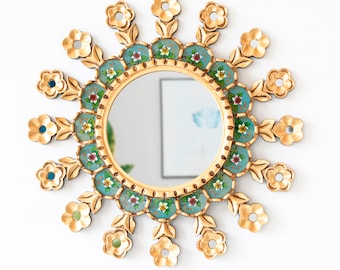 Op de afbeelding: Een ronde gouden spiegel met een decoratief bloemenontwerp. De spiegel is omgeven door een ring van blauwe en groene geschilderde bloemen met gouden accenten. De spiegel is perfect om elke kamer een vleugje elegantie te geven.