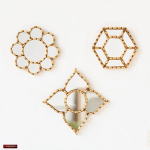 May include: Three gold-toned decorative mirrors with geometric designs. The mirrors are arranged in a triangular pattern on a white wall.