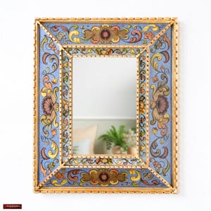 May include: A rectangular mirror with a gold-coloured frame and intricate floral patterns. The frame has a light blue background with detailed designs in yellow, orange, and brown. The mirror's design is symmetrical and decorative, suitable for a wall.