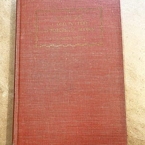 May include: A vintage book with a red cover and gold lettering. The title reads "Handbook of Old Pottery and Porcelain Marks" by Jordan Thorne. The cover has a textured appearance.