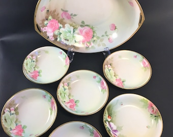 May include: A set of seven porcelain bowls with a delicate floral design. The bowls feature a light green background with pink roses and green leaves. The bowls have a gold rim and are perfect for serving snacks or desserts.