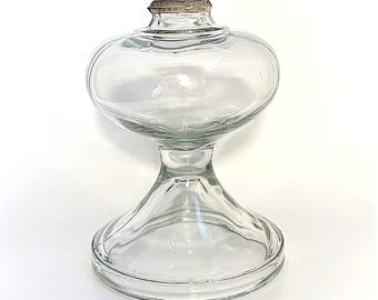 May include: A clear glass oil lamp with a round, bulbous top and a wide, flared base. The lamp has a simple, elegant design.
