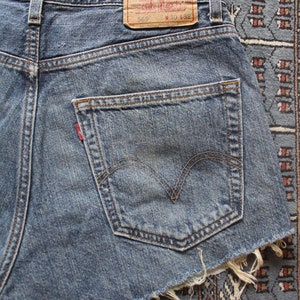 May include: A pair of blue denim shorts with a frayed hem. The shorts have a back pocket with a red Levi's tab and a brown leather patch with the text "Levi Strauss & Co. San Francisco, Cal.  Original  Quality  Clothing  Trade Mark  Registered  569  W 30 L 32".