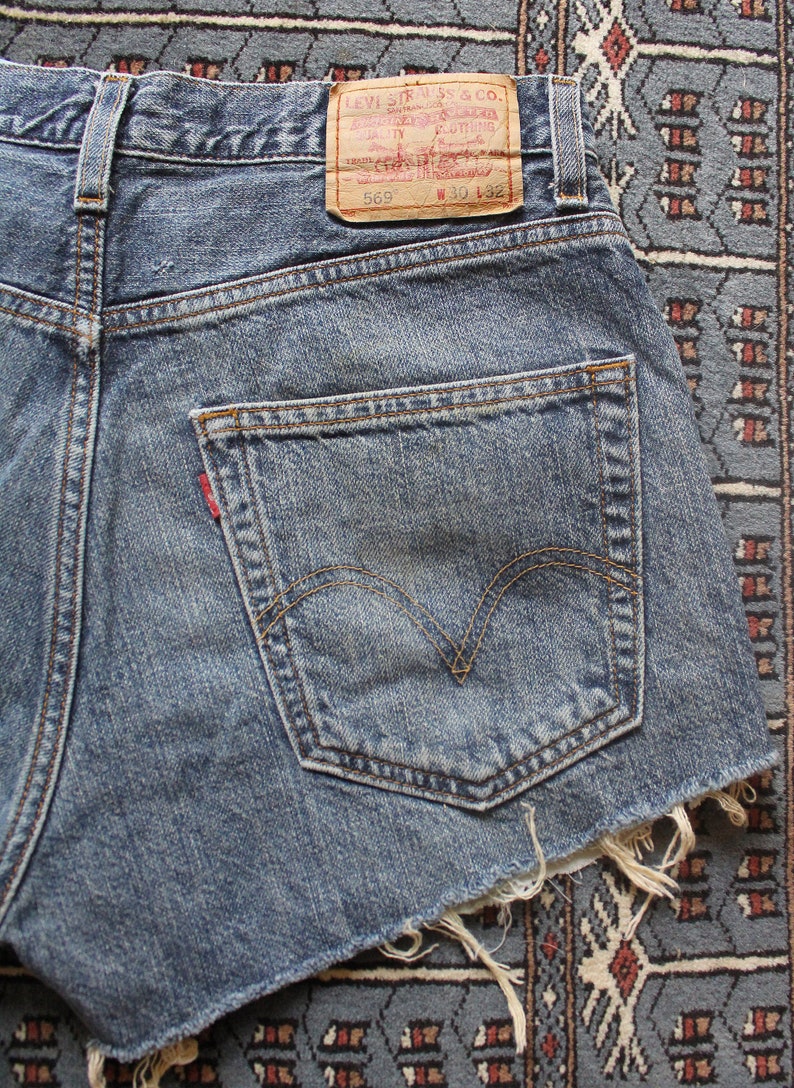 May include: A pair of blue denim shorts with a frayed hem. The shorts have a back pocket with a red Levi's tab and a brown leather patch with the text "Levi Strauss & Co. San Francisco, Cal.  Original  Quality  Clothing  Trade Mark  Registered  569  W 30 L 32".