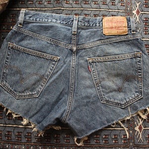May include: A pair of blue denim shorts with frayed edges. The shorts have two back pockets and a red leather patch with the text "Levi's" on the back.