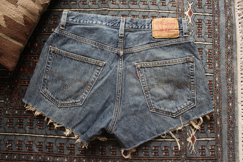 May include: A pair of blue denim shorts with frayed edges. The shorts have two back pockets and a red leather patch with the text "Levi's" on the back.