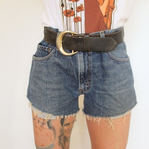 May include: A pair of blue denim shorts with frayed edges. The shorts are worn with a brown leather belt with a gold buckle.